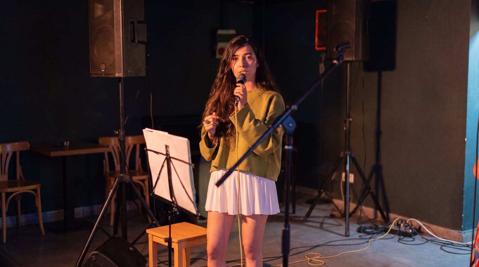 Olivia Mihet cântând la microfon, într-un pulover verde, sub o lumină caldă de scenă