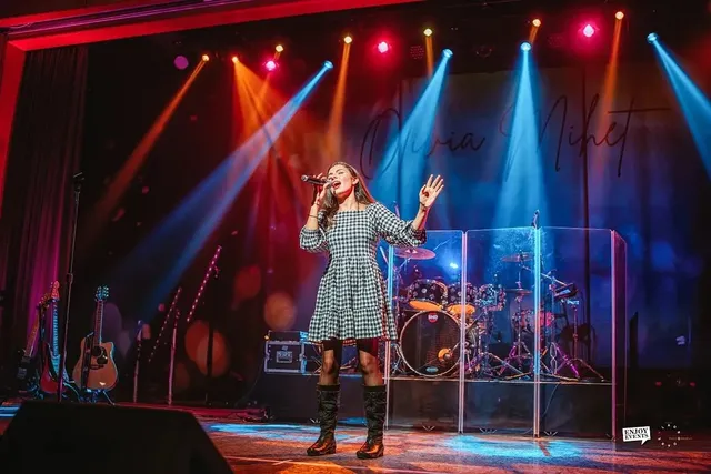 Scenă completă de concert cu echipament de trupă, lumini colorate și un fundal cu semnătura sa scrisă de mână