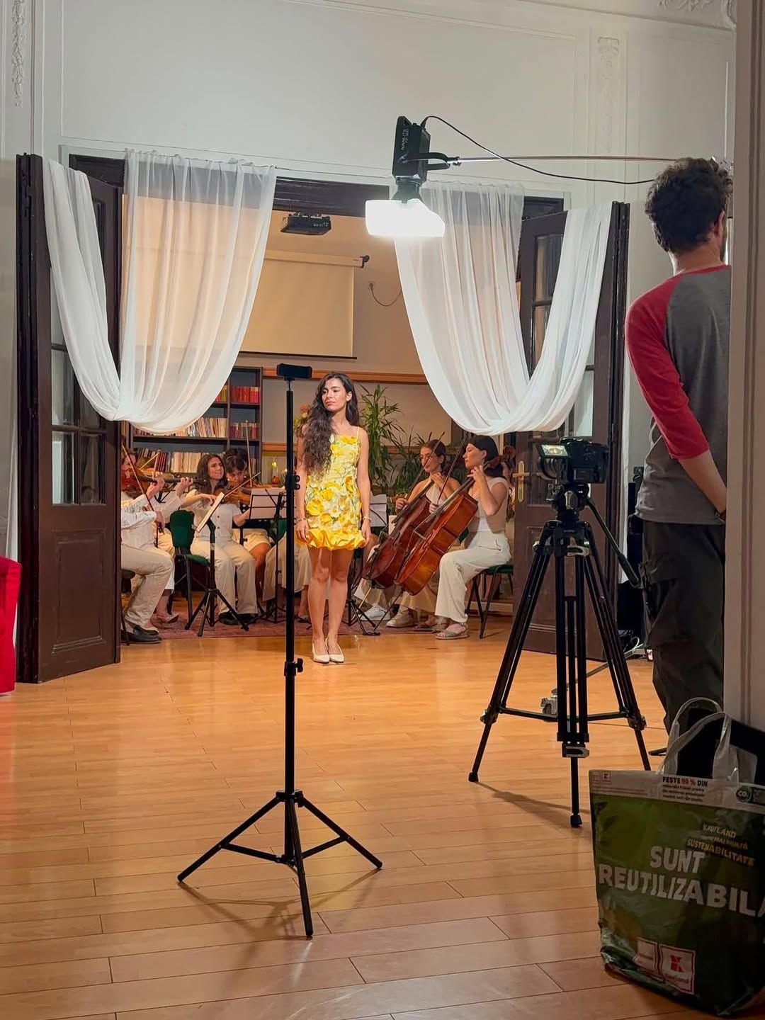 Cadru din culisele unei filmări, cu echipament de cameră, Olivia în rochia galbenă cu model floral în plan secund