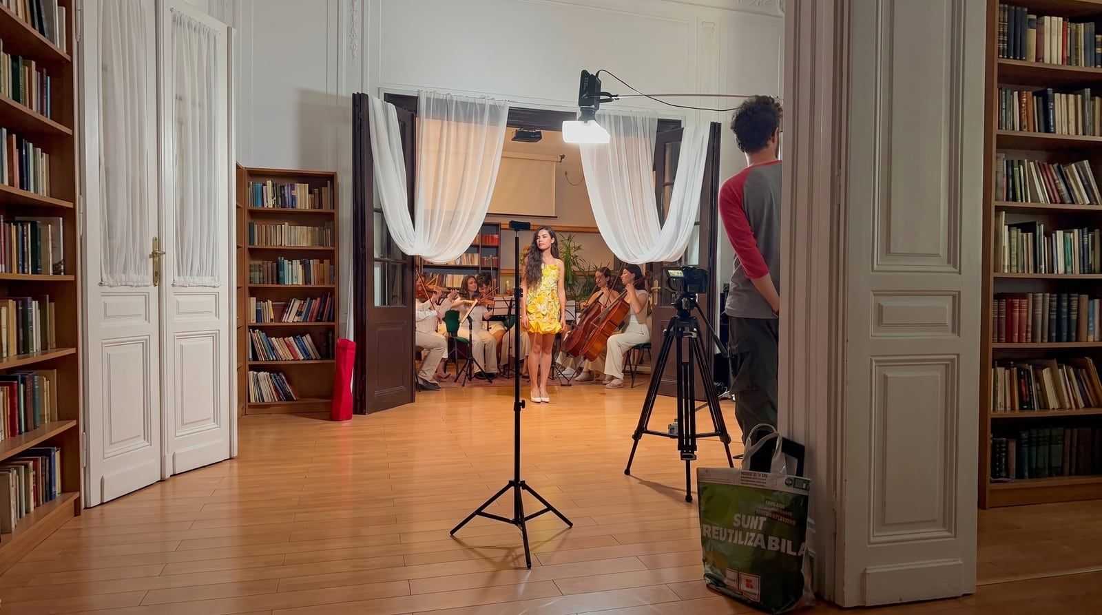 Behind-the-scenes shot of a video shoot with camera rig, Olivia in the yellow floral dress in the background